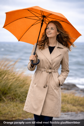 Kvindelig med orange paraply ved kysten
